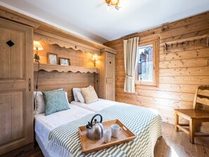 A cozy wooden room with a bed, a wooden chair, and a window with curtains. - Bright apartment near the slopes (Les Menuires)