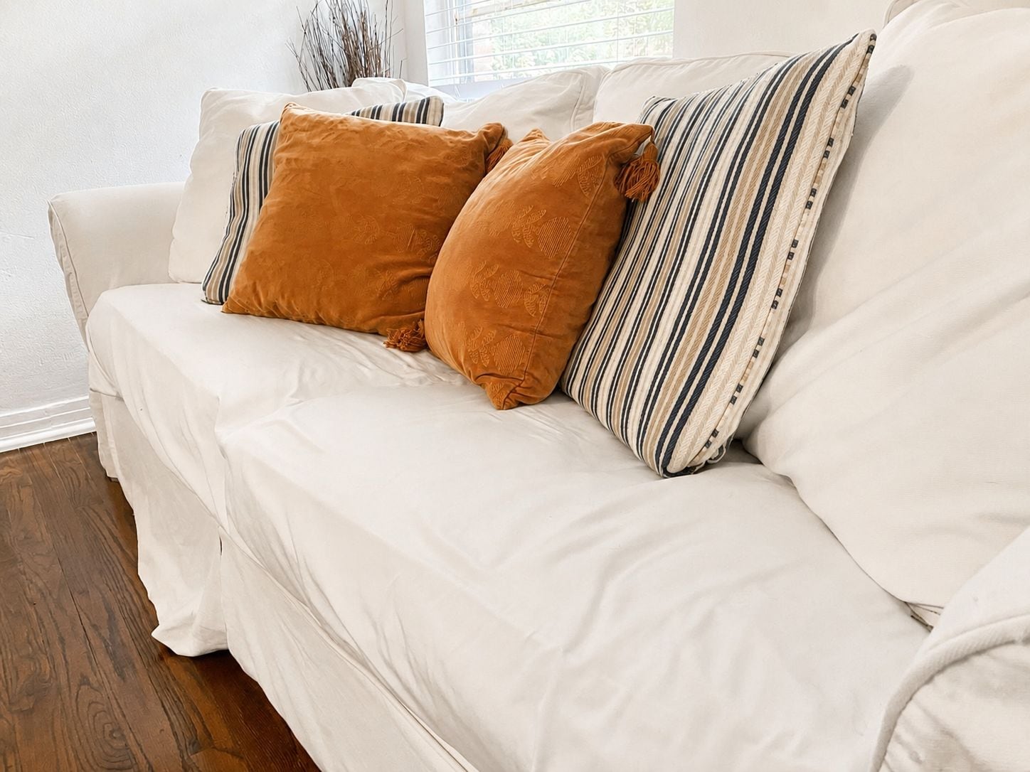 A white sofa with two brown cushions and a striped pillow.