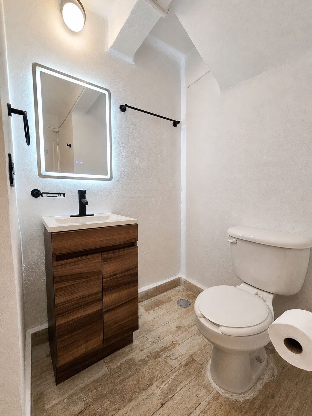 Un baño con tocador de madera, un espejo, un inodoro y un perchero para toallas.