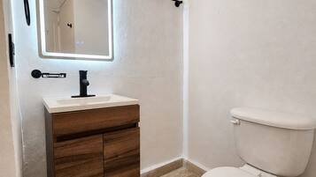 Un baño con tocador de madera, un espejo, un inodoro y un perchero para toallas.