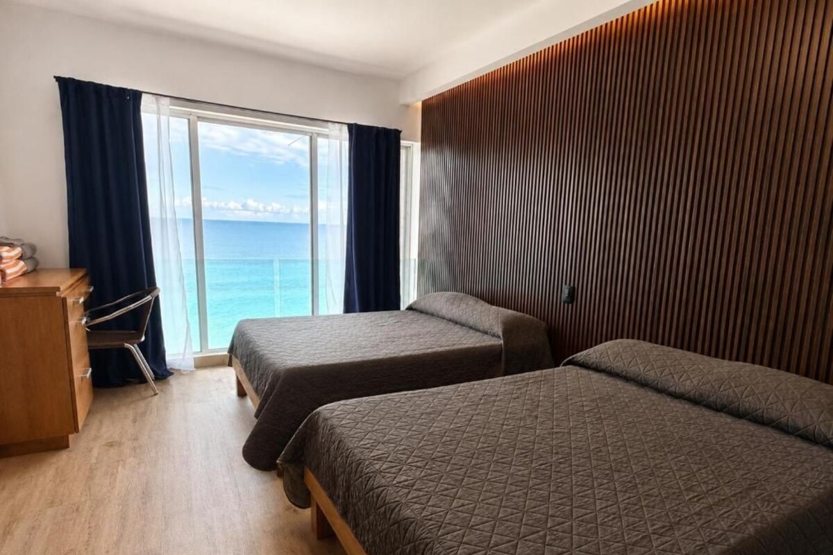 Quarto de hotel com duas camas, uma escrivaninha e vista para o mar.
