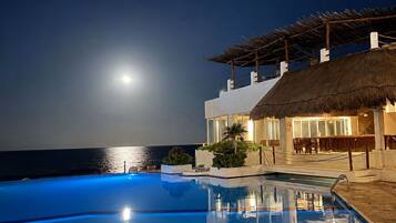 A nighttime pool area with a clear view of the ocean and a full moon.