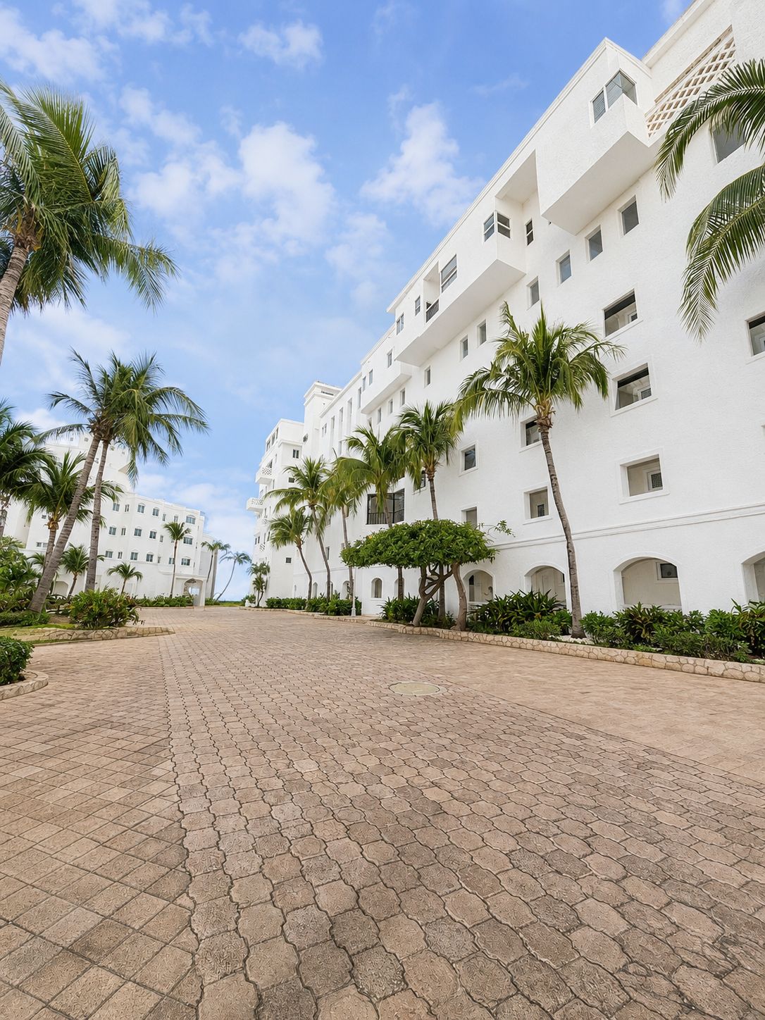 Um hotel com vários andares, pátio pavimentado e palmeiras.
