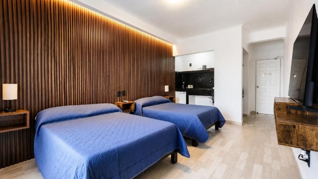 Ein Hotelzimmer mit zwei Betten, einer Holzwand, einem Fernseher und einer Küchenzeile.