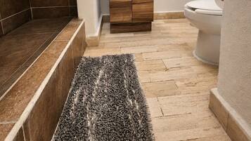 Ein Badezimmer mit einem Holzkosmetikschrank, einem beleuchteten Spiegel, einer Toilette und einer Duschkabine.