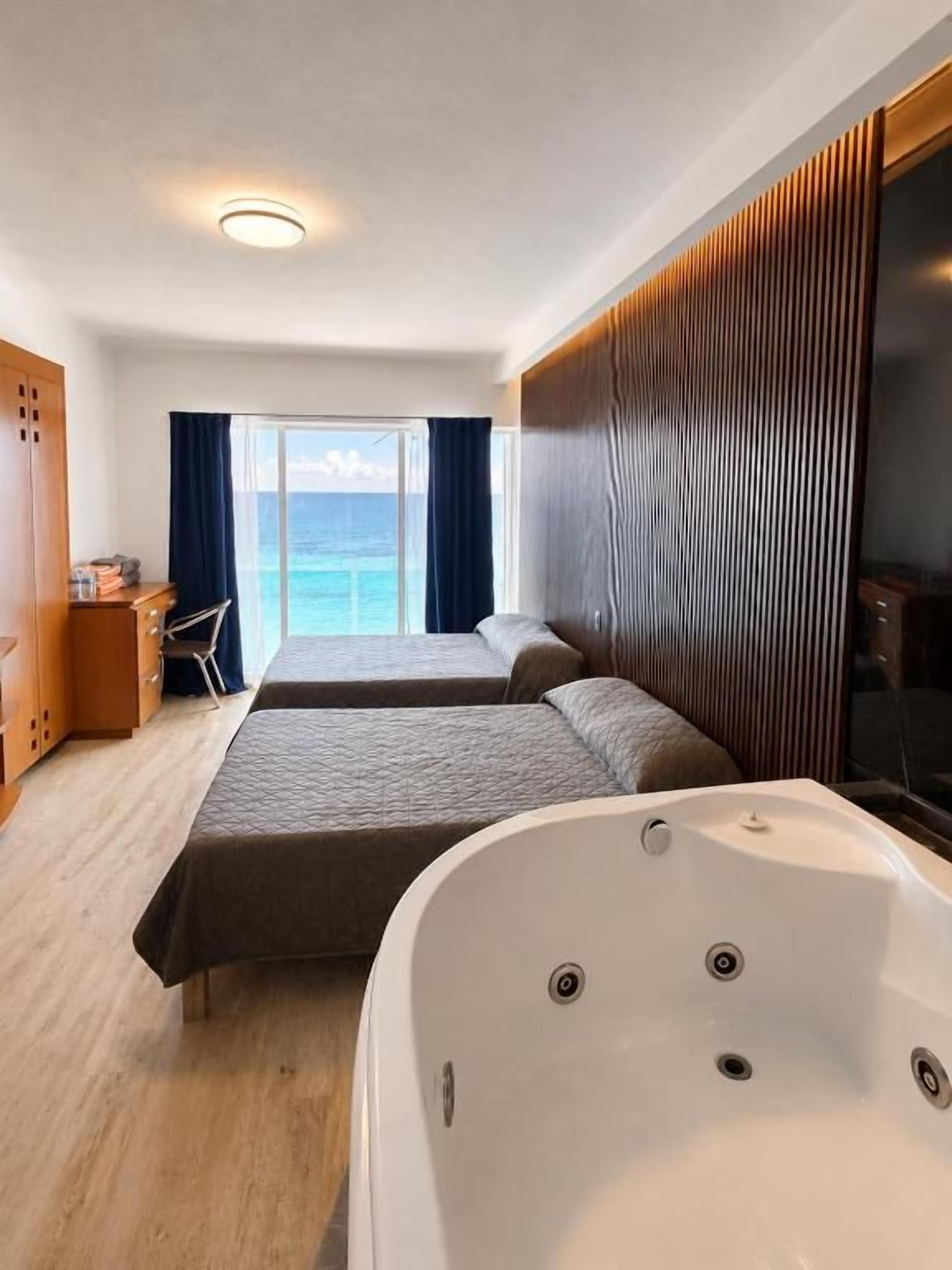 Ein Hotelzimmer mit zwei Betten, einer großen Badewanne und Meerblick.