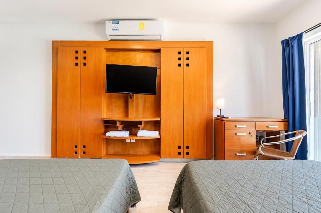 A hotel room with two beds, a wardrobe, a desk, a chair, and a television.