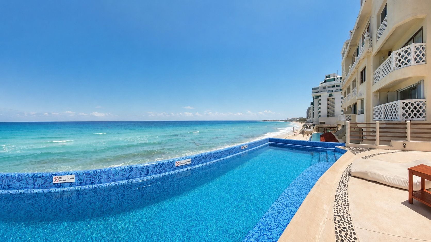Ein Pool mit klarem, blauen Rand, neben einem Strand und Hotelgebäuden.