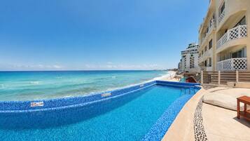 Ein Pool mit klarem, blauen Rand, neben einem Strand und Hotelgebäuden.