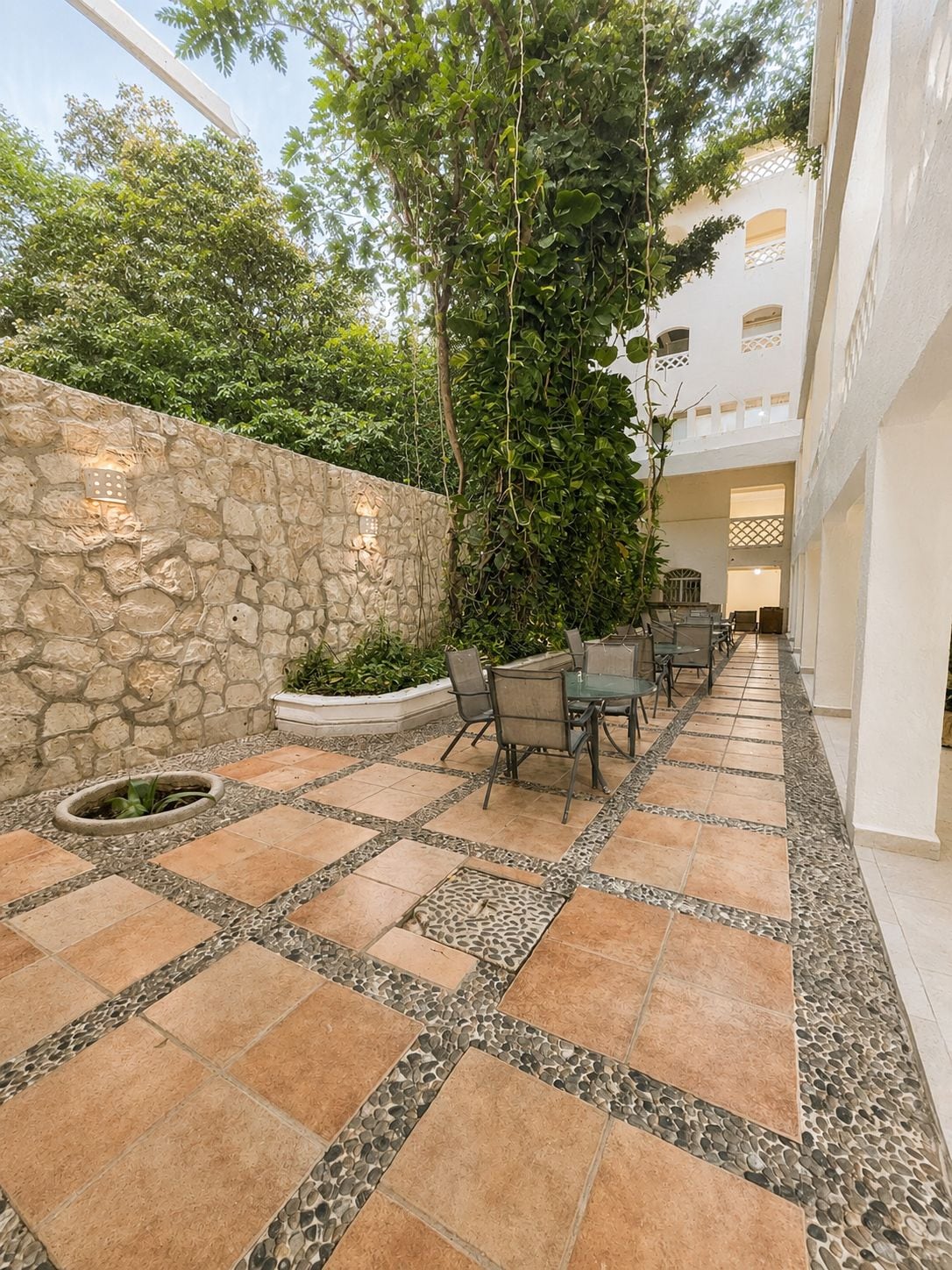 A courtyard with stone walls, a seating area with chairs and a table, and a potted plant.