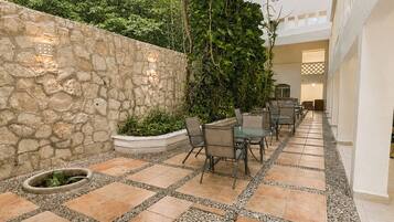 A courtyard with stone walls, a seating area with chairs and a table, and a potted plant.