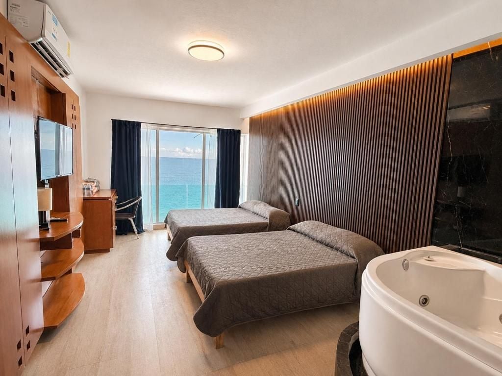 Ein Hotelzimmer mit zwei Betten, einer Sitzecke, einem großen Fenster mit Blick, einer Badewanne und einem Holzschrank.