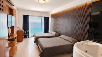 Ein Hotelzimmer mit zwei Betten, einer Sitzecke, einem großen Fenster mit Blick, einer Badewanne und einem Holzschrank.