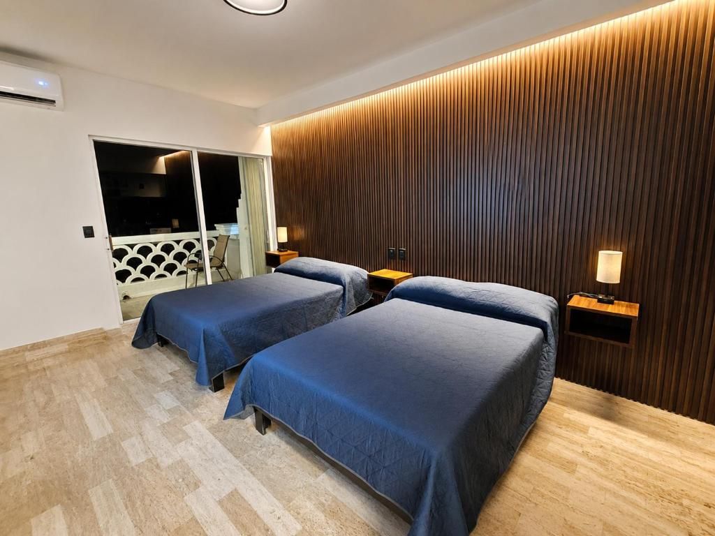 A hotel room with two beds, a wooden wall paneling, and a view of a balcony.