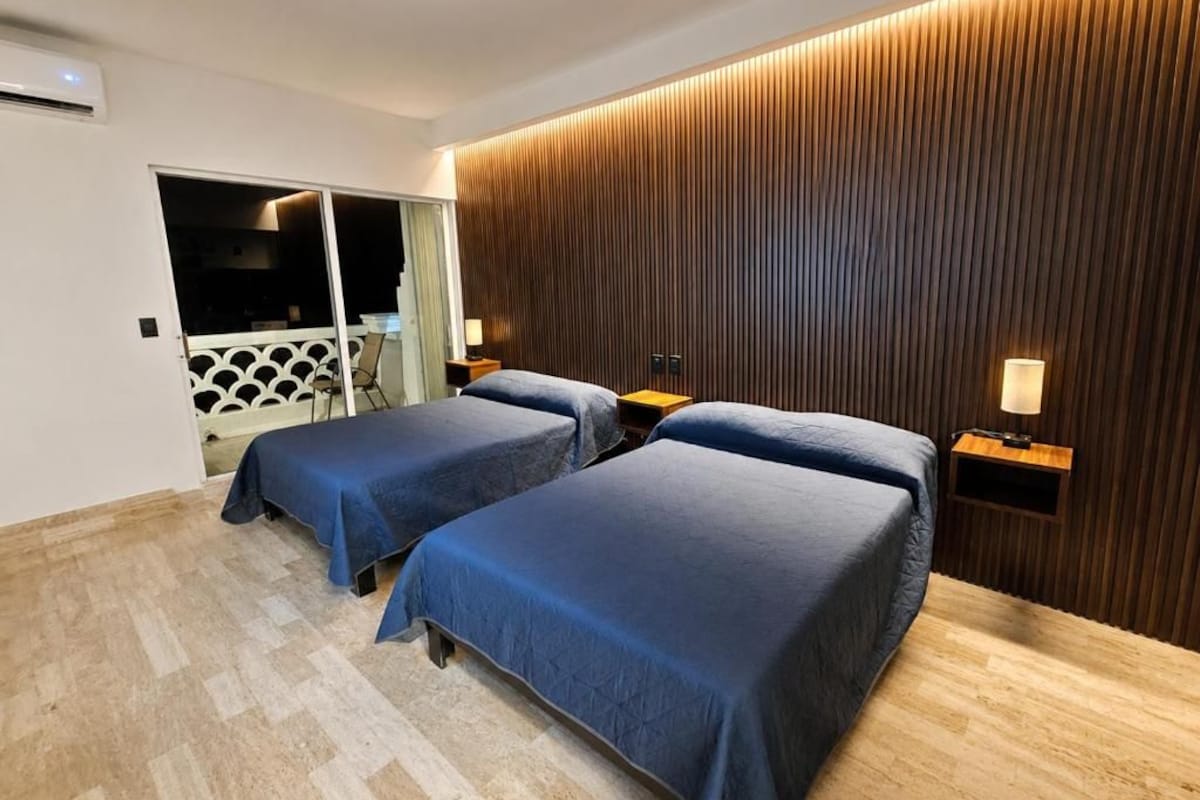 Quarto de hotel com duas camas, painel de parede de madeira e vista para uma varanda.