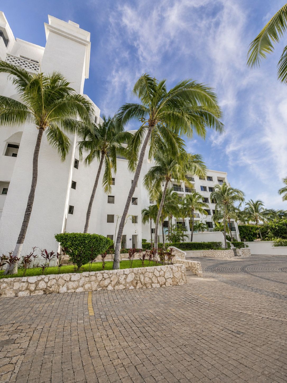 Um hotel com fachada branca, palmeiras e um pátio pavimentado.