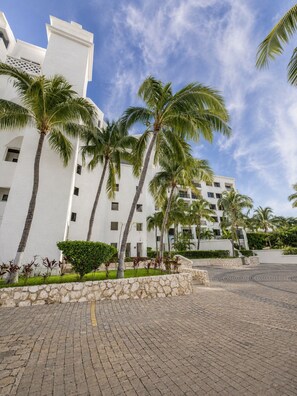 Um hotel com fachada branca, palmeiras e um pátio pavimentado.