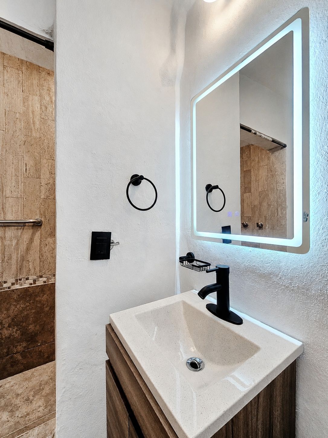Casa de banho com lavatório branco, torneira preta e espelho com iluminação integrada.