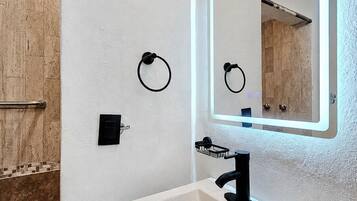 Casa de banho com lavatório branco, torneira preta e espelho com iluminação integrada.