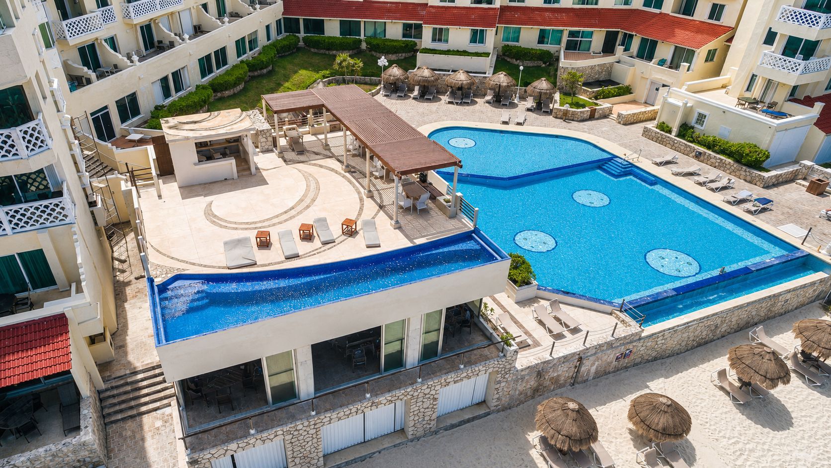 A hotel with a large outdoor swimming pool, sun loungers, and a covered seating area.