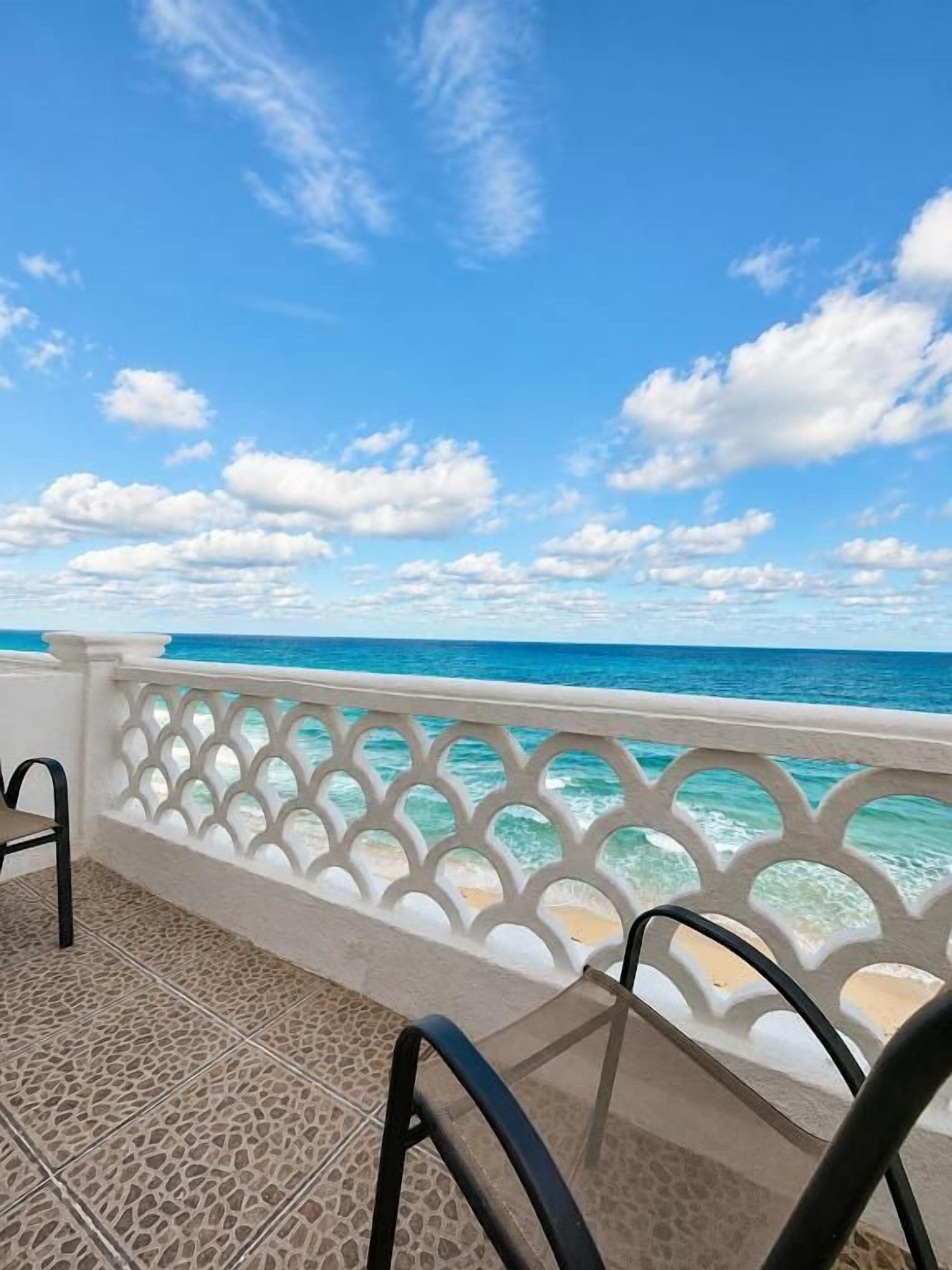 Varanda com vista para o oceano, grade branca e chão de azulejos.