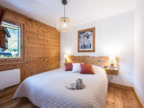 Een slaapkamer met een houten hoofdeinde, een bed met een witte sprei, nachtlampjes, een raam met uitzicht en een lijst met een afbeelding aan de muur.