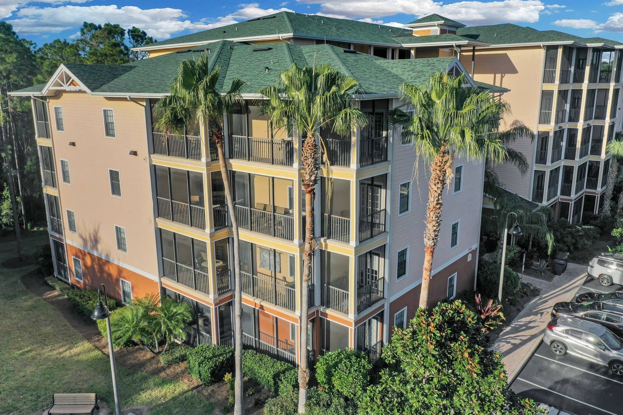 A multi-story hotel with balconies, a parking lot, and surrounding greenery.