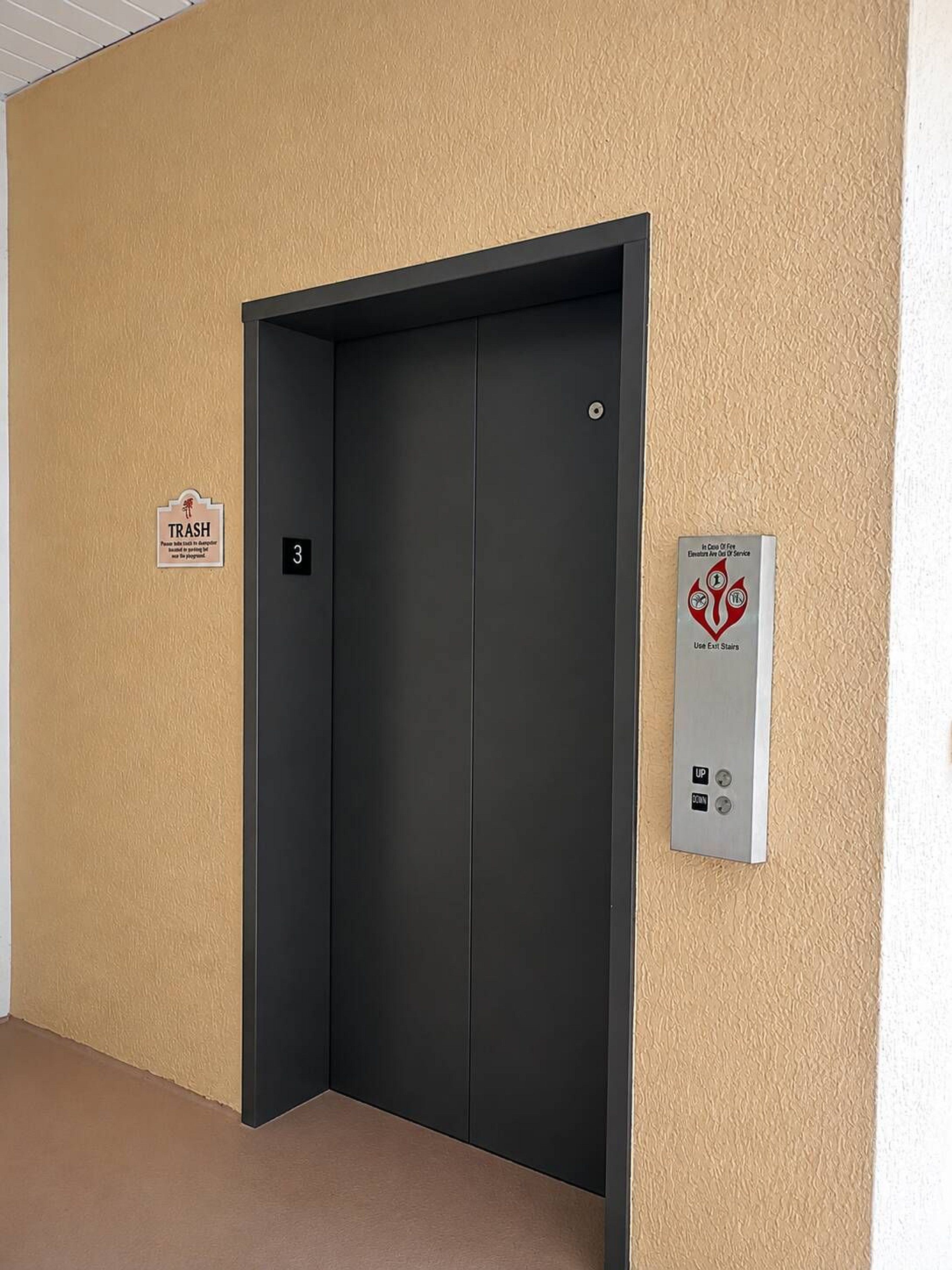 Eine geschlossene Aufzugtür mit einem 'Müll'-Schild und einem Brandschutznachweis an der Wand.