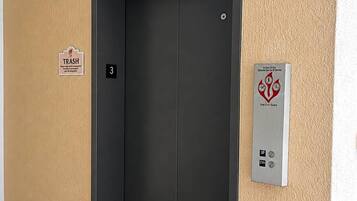 Eine geschlossene Aufzugtür mit einem 'Müll'-Schild und einem Brandschutznachweis an der Wand.