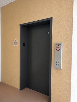 Eine geschlossene Aufzugtür mit einem 'Müll'-Schild und einem Brandschutznachweis an der Wand.