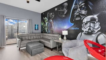 A modern living room with a sectional sofa, a red chair, a small table with a lamp, and a Star Wars-themed mural on the wall.