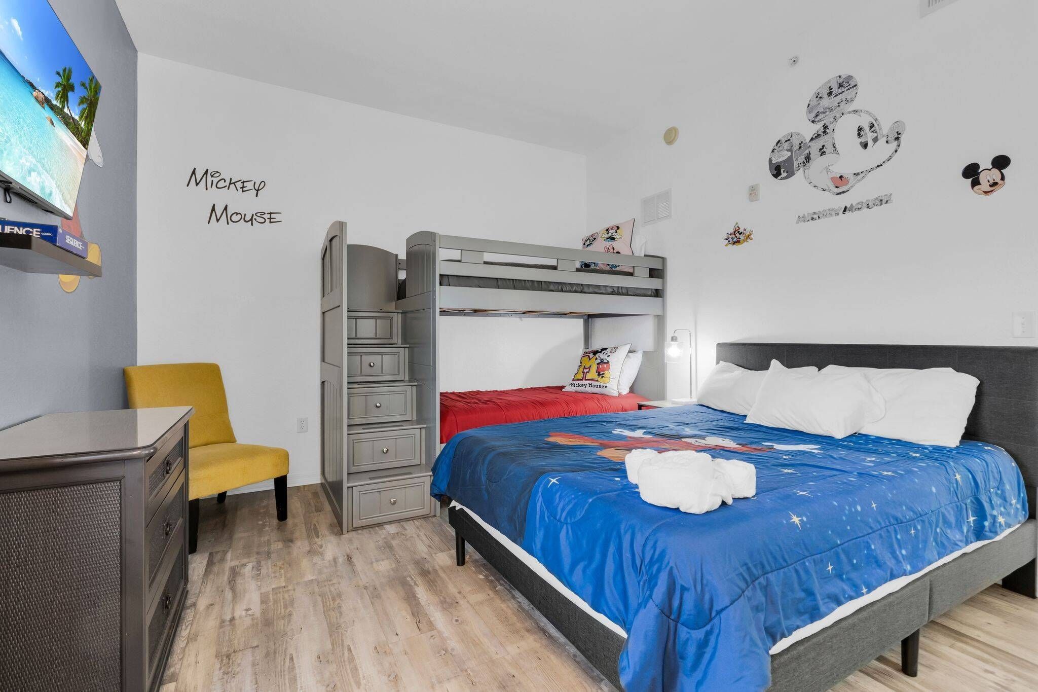 A room with a bunk bed, a desk, a chair, and wall decorations including Mickey Mouse.
