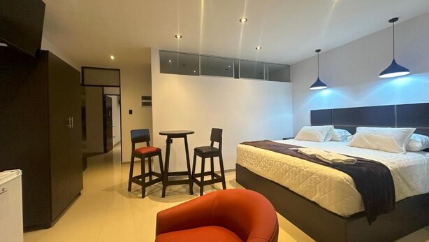 A modern hotel room with a large bed, a red chair, a small table, and a minibar. - Vista a Mar (Aucallama)