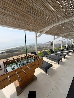 A rooftop terrace with a foosball table, lounge chairs, and a view of the coastline.