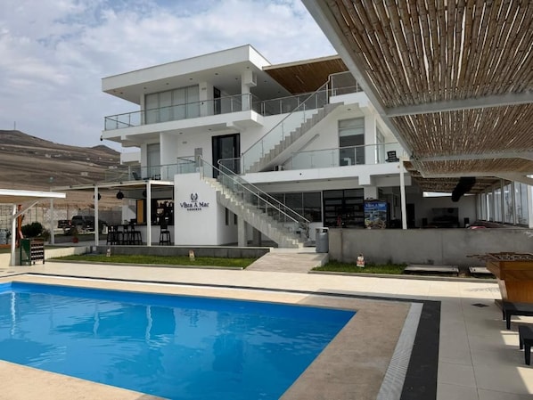 A modern hotel with a pool, outdoor seating, and a staircase leading to the upper floors. - Vista a Mar (Aucallama)