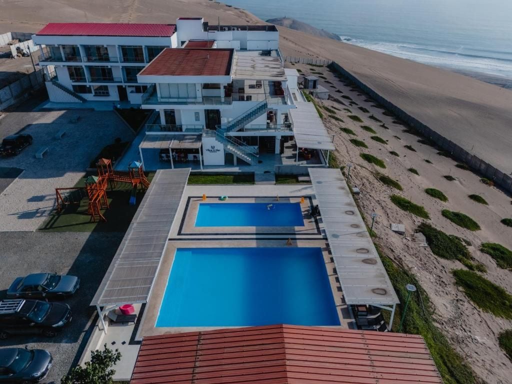 Um imóvel à beira-mar com piscina, varanda coberta e um edifício de vários andares com telhado vermelho.