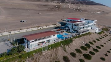 A modern hotel with a pool, located on a hillside with a desert landscape in the background.