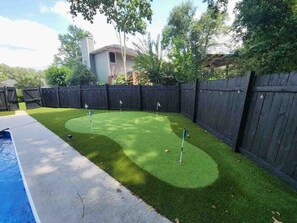 A backyard with artificial grass, a pool, and a wooden fence. - 4 BR/3 Bath Tuscaloosa Retreat With Pool, Hot Tub and Putting Green (Northport)