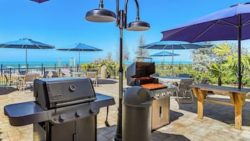 An outdoor patio with a grill, umbrellas, and a view of the ocean.