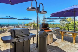 An outdoor patio with a grill, umbrellas, and a view of the ocean. - Vanderbilt Beach & Harbour Club (Naples)