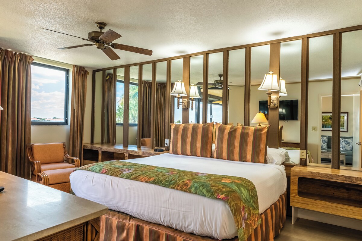 A hotel room with a bed, a desk, a chair, a television, and a ceiling fan.