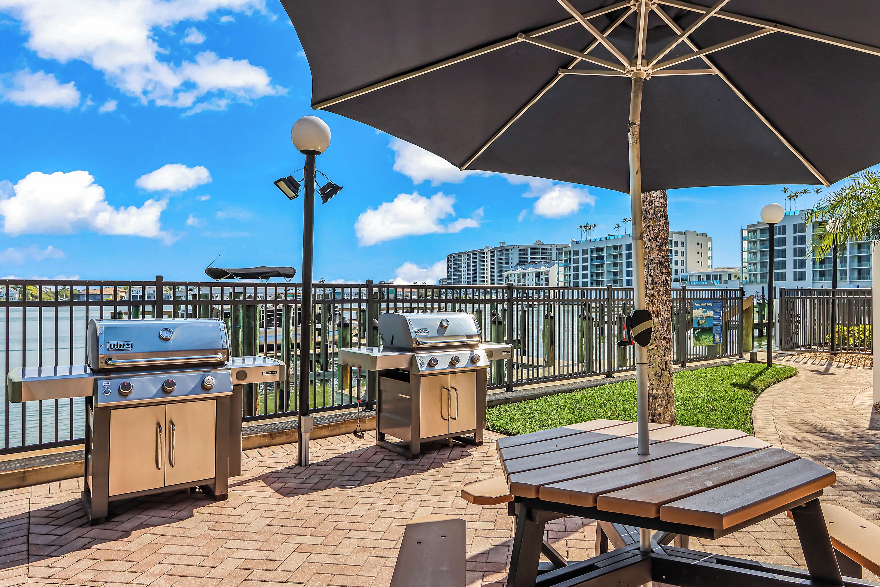 An outdoor patio area with barbecue grills, a picnic table, and a large umbrella providing shade.