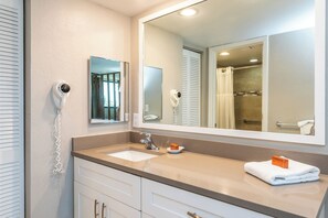 A bathroom with a sink, mirror, and a hairdryer mounted on the wall. - Vanderbilt Beach & Harbour Club (Naples)
