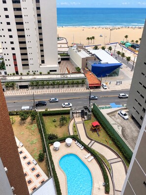 A high-rise building with a swimming pool, a beach, and a parking area. - No Melhor de Iracema ate 6 Pessoas (Fortaleza)
