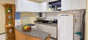 A kitchen with white cabinets, a granite countertop, a water dispenser, a stove, and a refrigerator. - No Melhor de Iracema ate 6 Pessoas (Fortaleza)