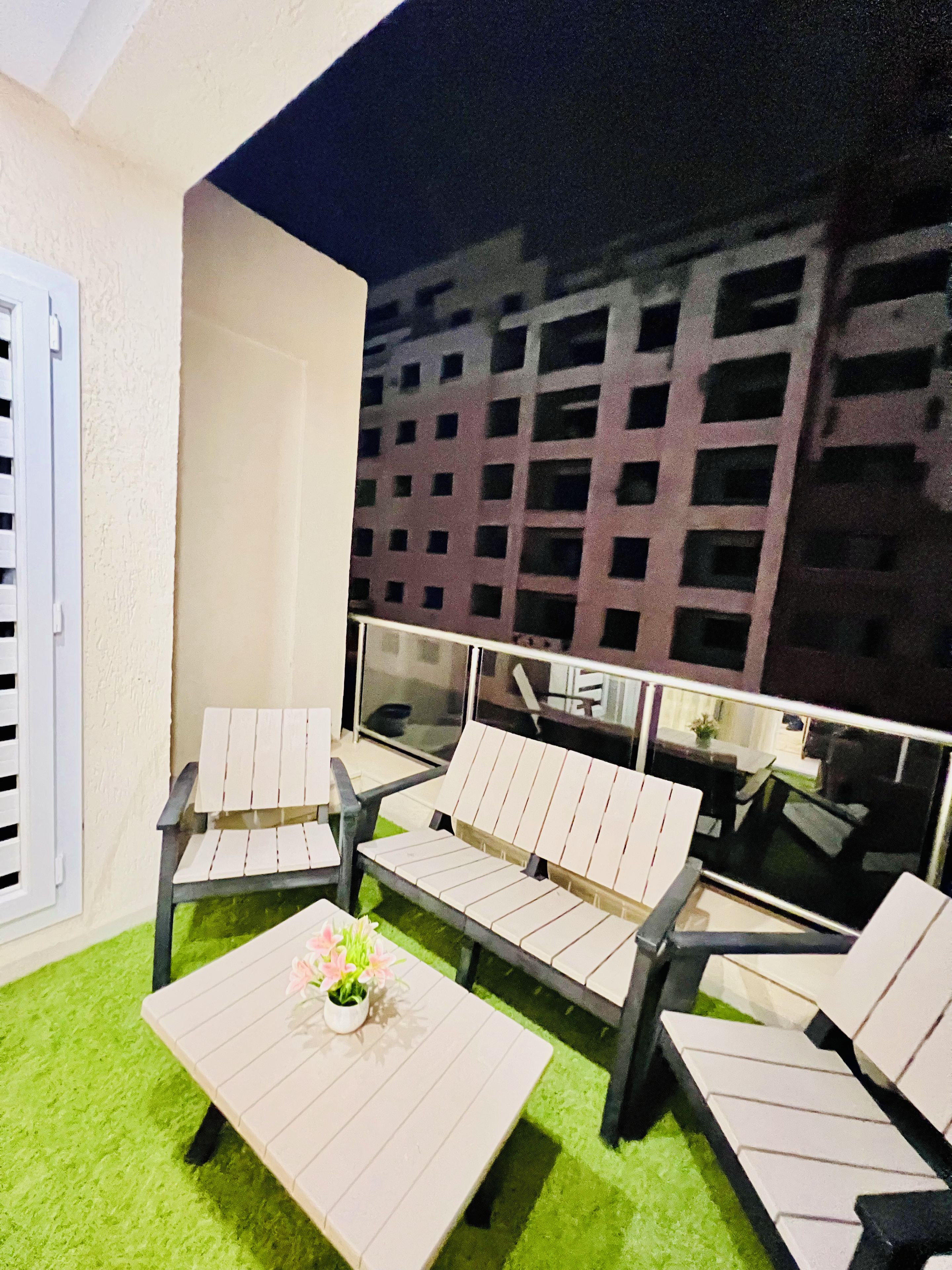 Un área de estar al aire libre con una mesa, sillas, un pequeño arreglo floral y vista a un edificio al fondo.