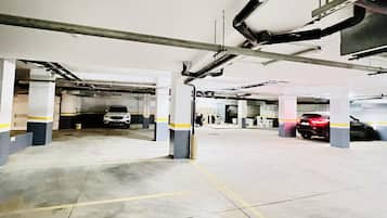 Een meerlaagse parkeergarage met betonnen vloeren en kolommen, met enkele geparkeerde voertuigen en zichtbare constructieelementen zoals leidingen en balken.