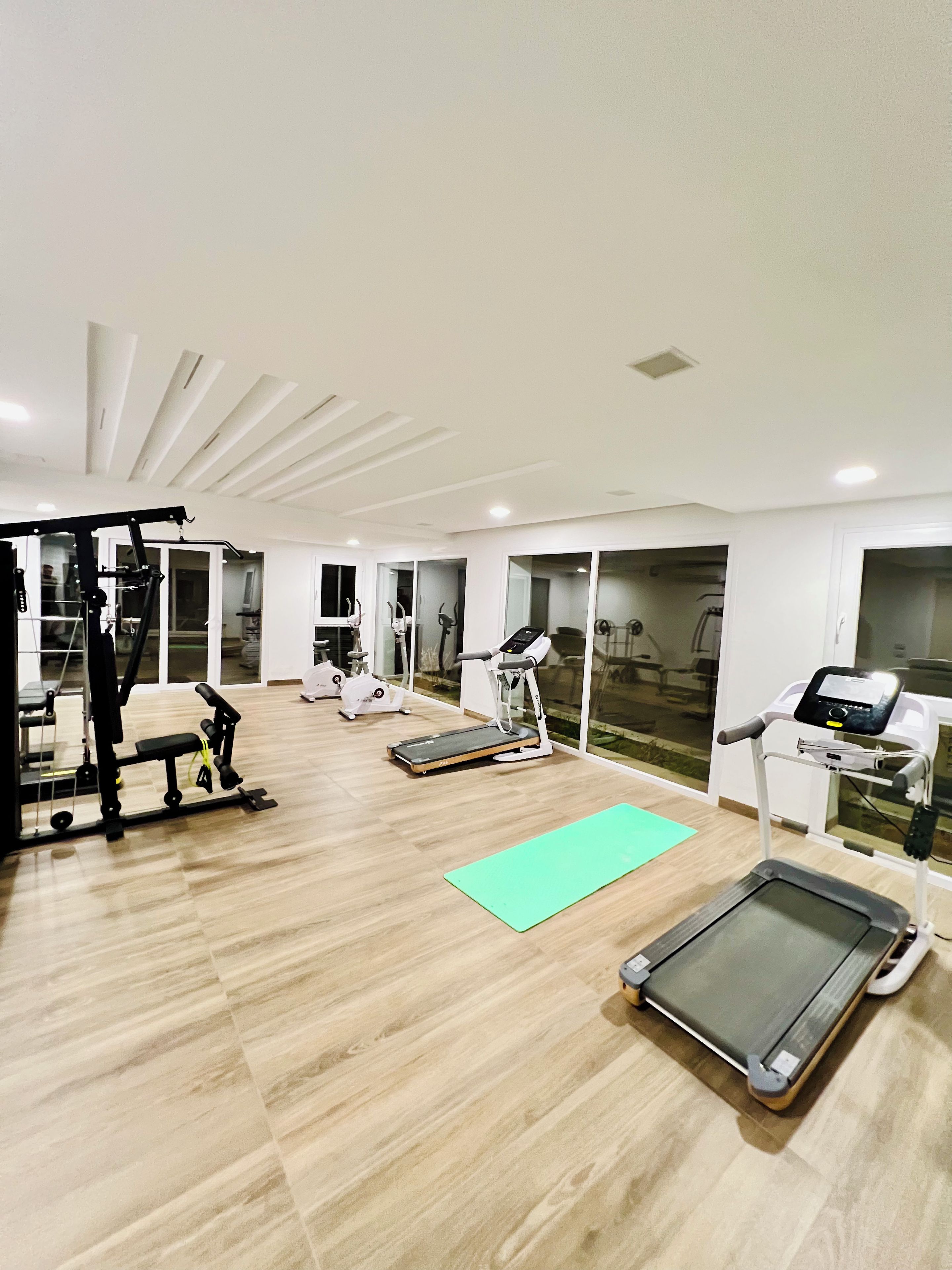 Ein Fitnessraum mit Trainingsgeräten, einer grünen Matte und einem Laufband.