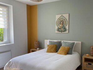 Ein Schlafzimmer mit einem Bett, einem Wandbild, einem Fenster und einem Nachttisch mit einer Lampe.
