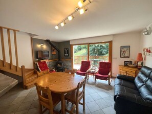 A cozy living room with a fireplace, a dining area with a wooden table and chairs, and a black leather sofa. - Charming duplex apartment - 6 guests (Valloire)